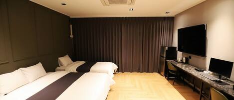 Habitación de hotel con dos camas, un escritorio con computadora, un televisor de pantalla plana y un refrigerador.