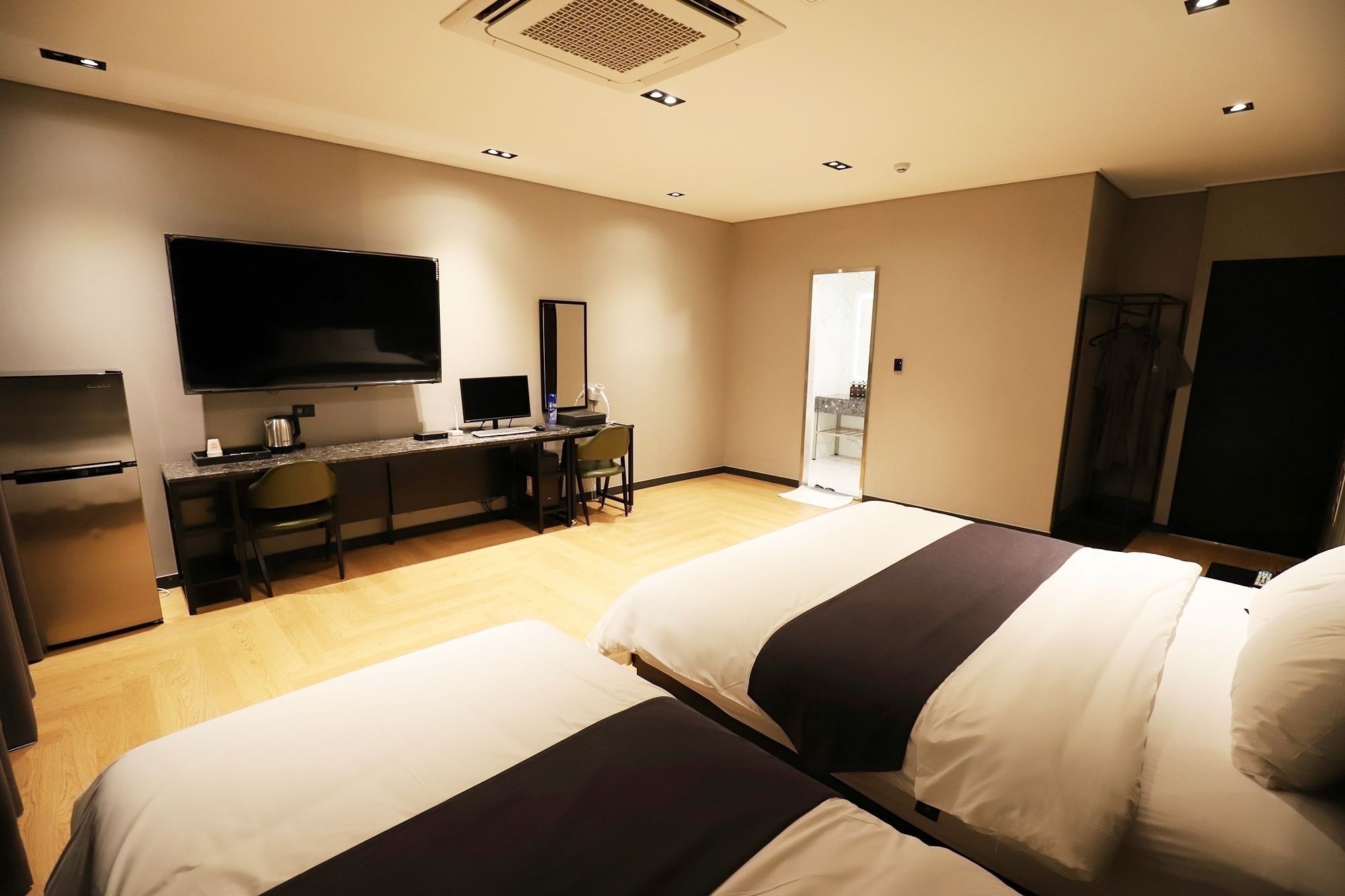 Habitación de hotel con dos camas, un escritorio con computadora, televisión y kitchenette.