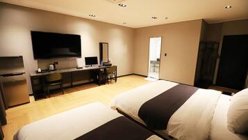 Habitación de hotel con dos camas, un escritorio con computadora, televisión y kitchenette.