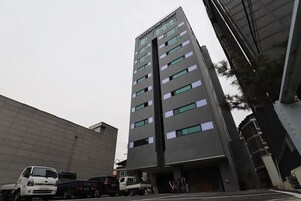 Un hotel de varios pisos con diseño moderno, que destaca por su entrada principal y numerosas ventanas.