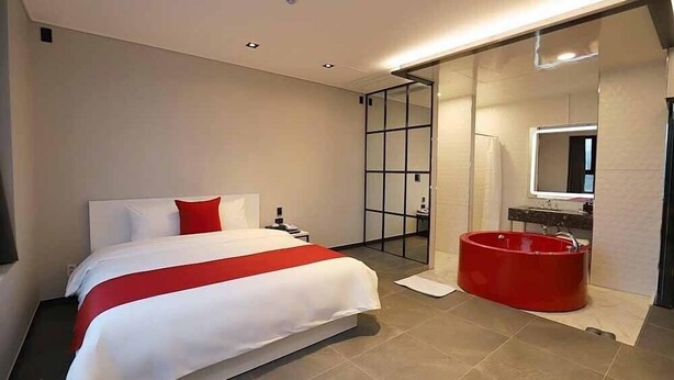Habitación de hotel moderna con una cama grande, pared de acento roja, separador de vidrio y una bañera roja.
