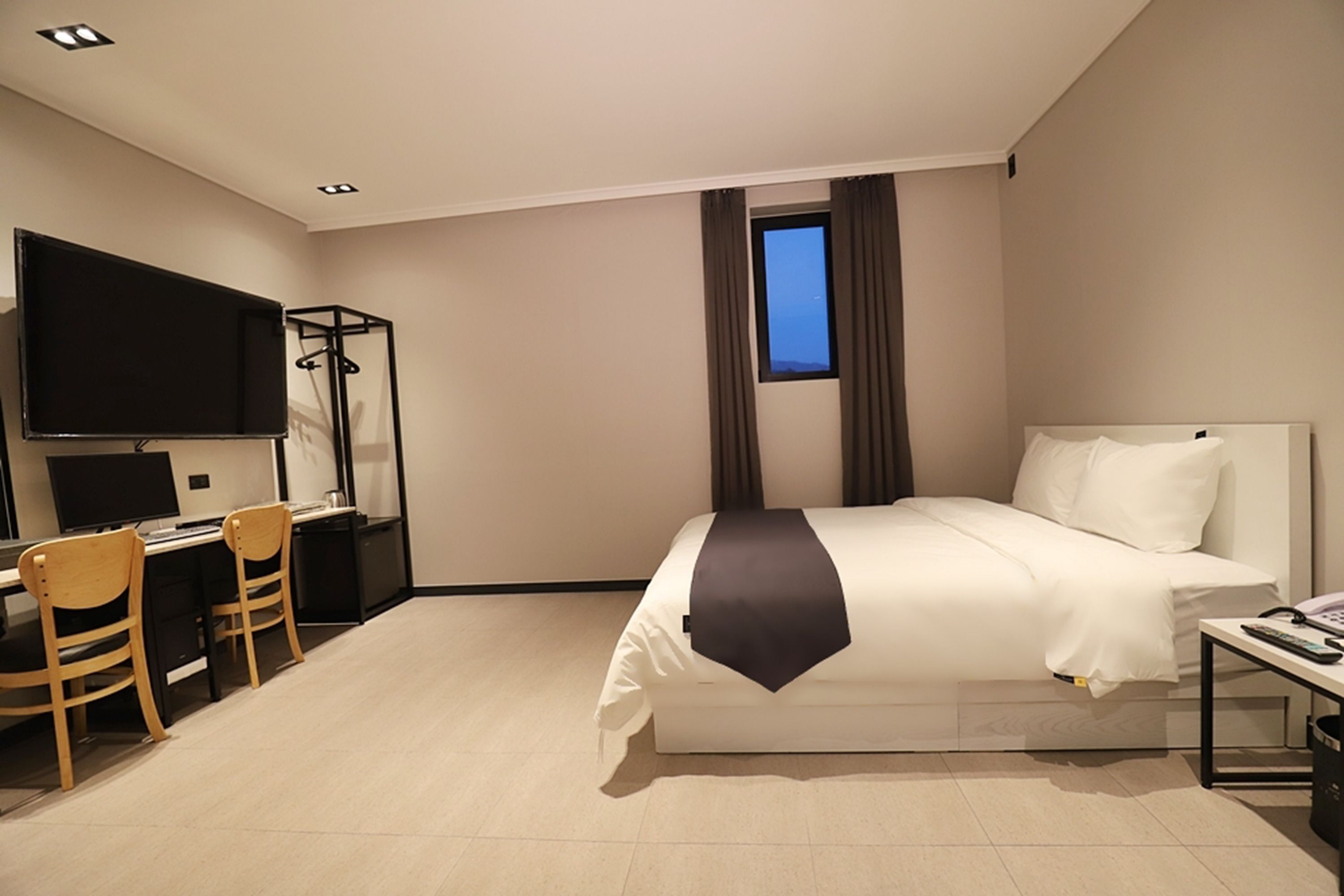 A hotel room with a bed, a desk with chairs, a TV, and a window with curtains.