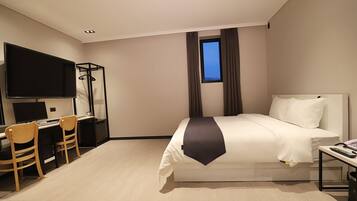 A hotel room with a bed, a desk with chairs, a TV, and a window with curtains.