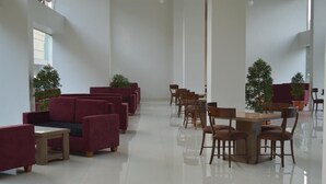 A spacious lobby with red sofas and wooden tables, potted plants, and a high ceiling. - Win Grand Hotel (Bekasi)