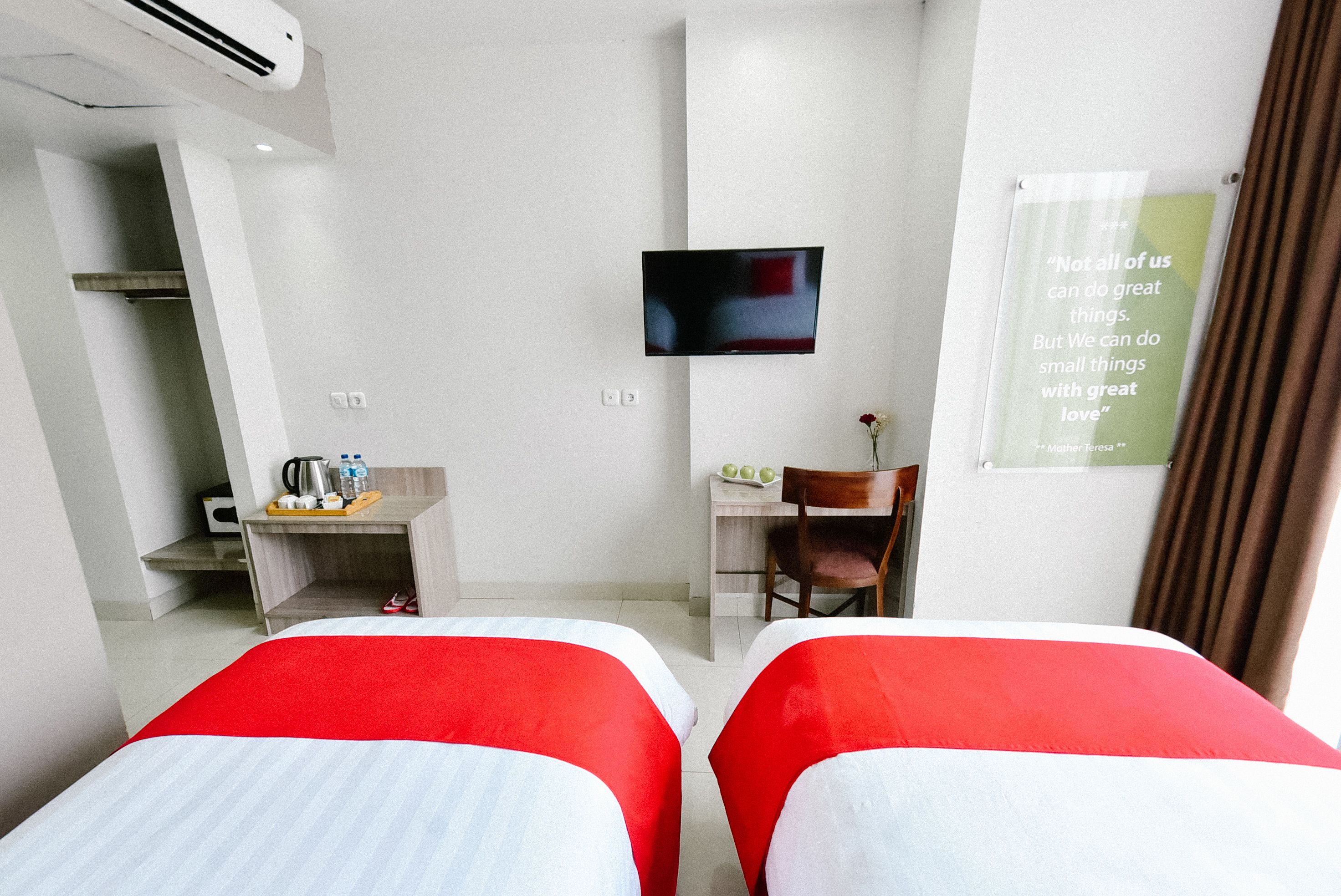 A hotel room with two beds, a TV, a desk with a chair, and a motivational quote on the wall.
