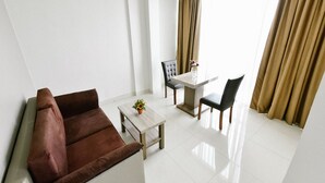 A modern living room with a brown sofa, a small table with a vase, and a dining area with chairs and a table. - Win Grand Hotel (Bekasi)