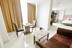 A hotel room with a bed, a desk with a chair, a coffee table, and a sofa. - Win Grand Hotel (Bekasi)