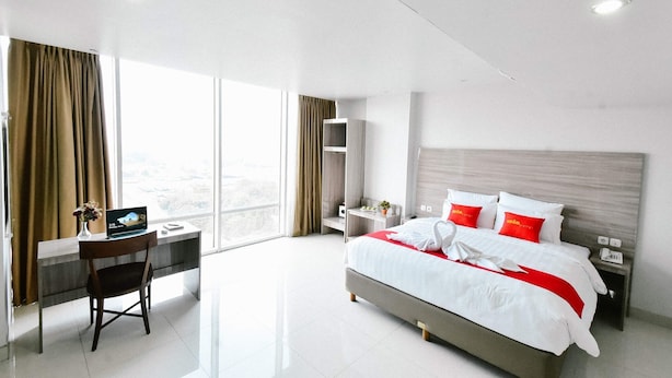 A modern hotel room with a large bed, a desk, and a view of the city. - Win Grand Hotel (Bekasi)