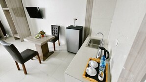 A modern kitchen with a dining area, a flat-screen TV mounted on the wall, a small refrigerator, and a sink with a kettle. - Win Grand Hotel (Bekasi)