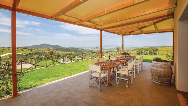 Un espace extérieur abrité, aménagé pour les repas, offrant une vue sur des collines verdoyantes et un vignoble.