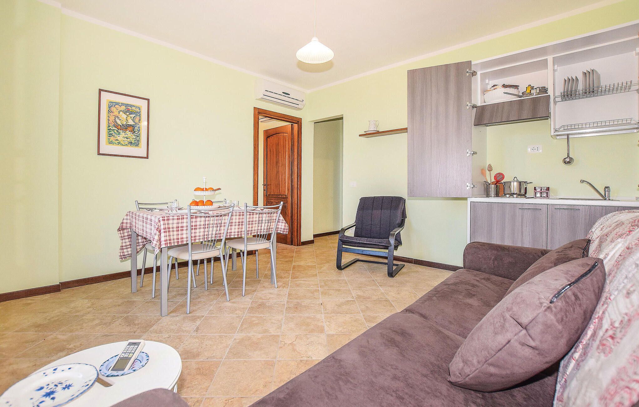 A living room with a brown sofa, a dining table with chairs, and a kitchen area with cabinets and a sink.