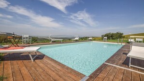 Une piscine d’un bleu éclatant, bordée d’une terrasse en bois, dotée de chaises longues et offrant une vue magnifique sur des collines et des montagnes.
