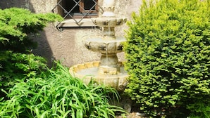 A stone fountain with multiple tiers, surrounded by lush greenery and a stone wall.