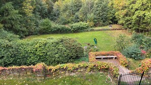 A lush garden with a variety of trees and shrubs, a stone wall with climbing plants, and a bench.