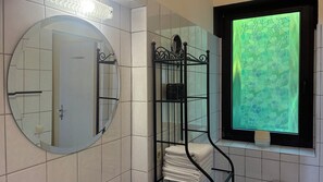 A bathroom with a round mirror, a towel rack, and a window with a green leafy pattern.