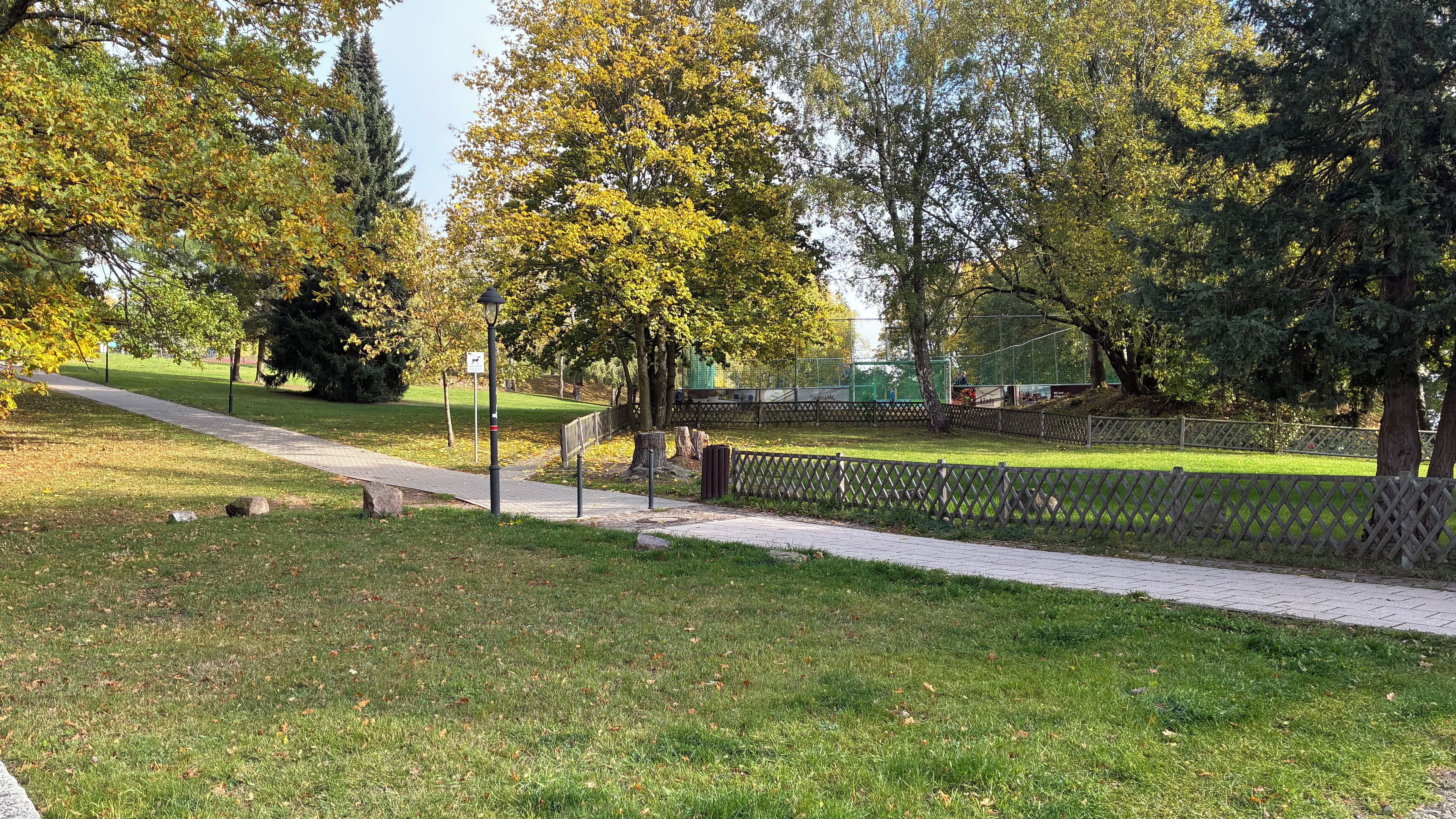 Ein Park mit einem gepflasterten Weg, Bäumen und einem eingezäunten Bereich.