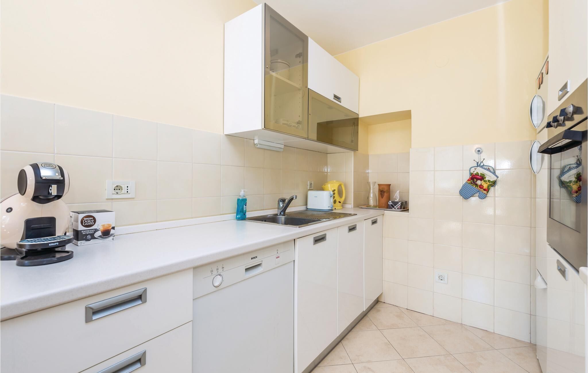 Een moderne keuken met witte kastjes, een Bosch vaatwasser, een koffieapparaat en een spoelbak.