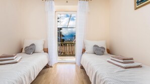 Un dormitorio con dos camas, ropa de cama blanca y vistas a un balcón con barandilla.