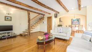 Una sala de estar con escalera de madera, televisor de pantalla plana, mesa de centro de vidrio y sofá blanco.