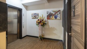 A hallway with an elevator, a floral arrangement, and two abstract paintings on the wall. - Front One Boutique Karawang (Karawang)