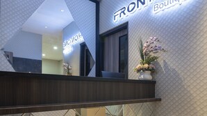 A reception area with a marble floor, a dark reception desk, and a wall with the text "FRONTONE Boutique". - Front One Boutique Karawang (Karawang)