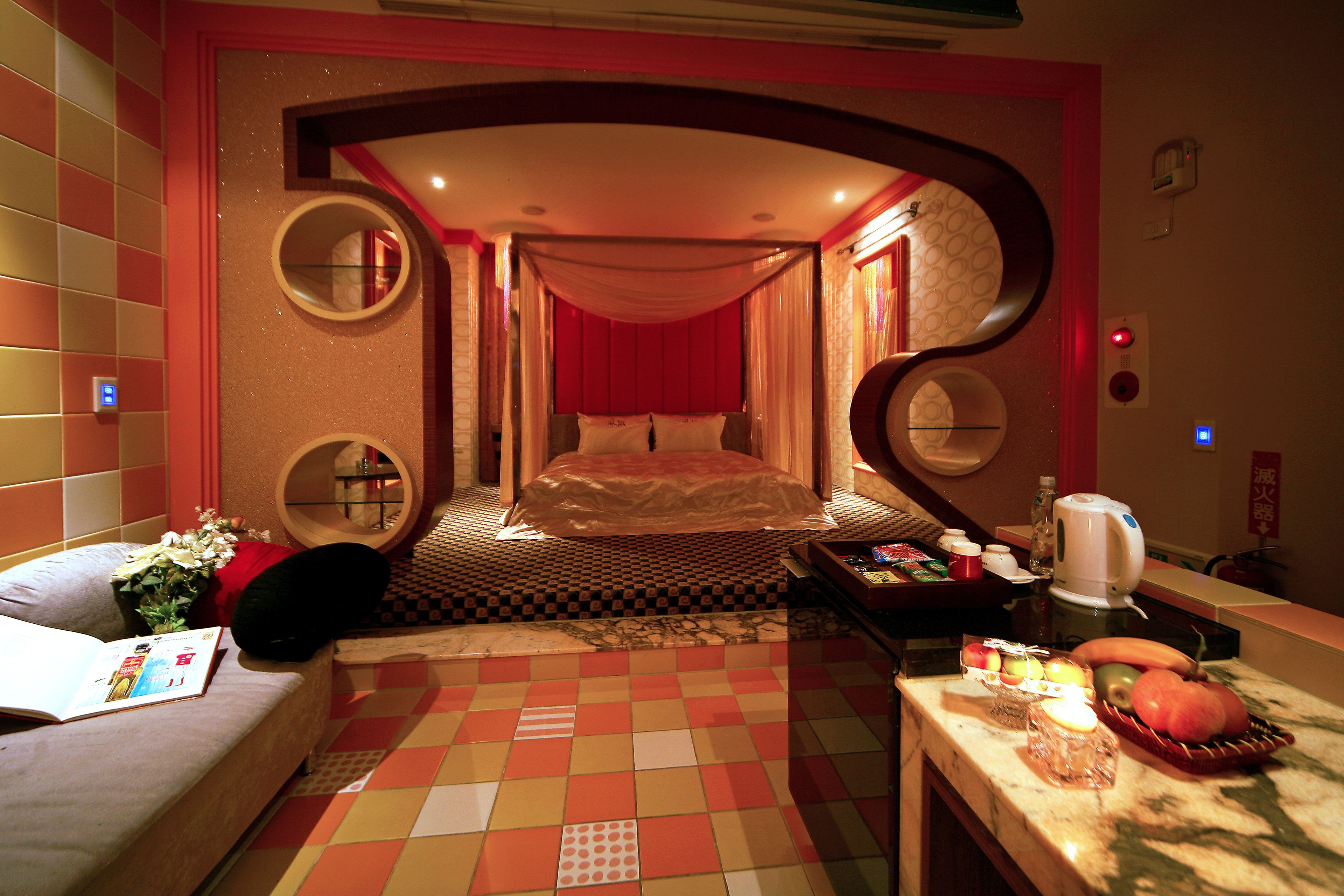 A hotel room with a bed, a sofa, a dining table with fruits, and a mirror.