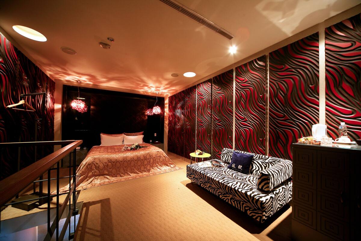 A modern bedroom with a bed, a zebra-patterned sofa, a small round table, and a dresser.