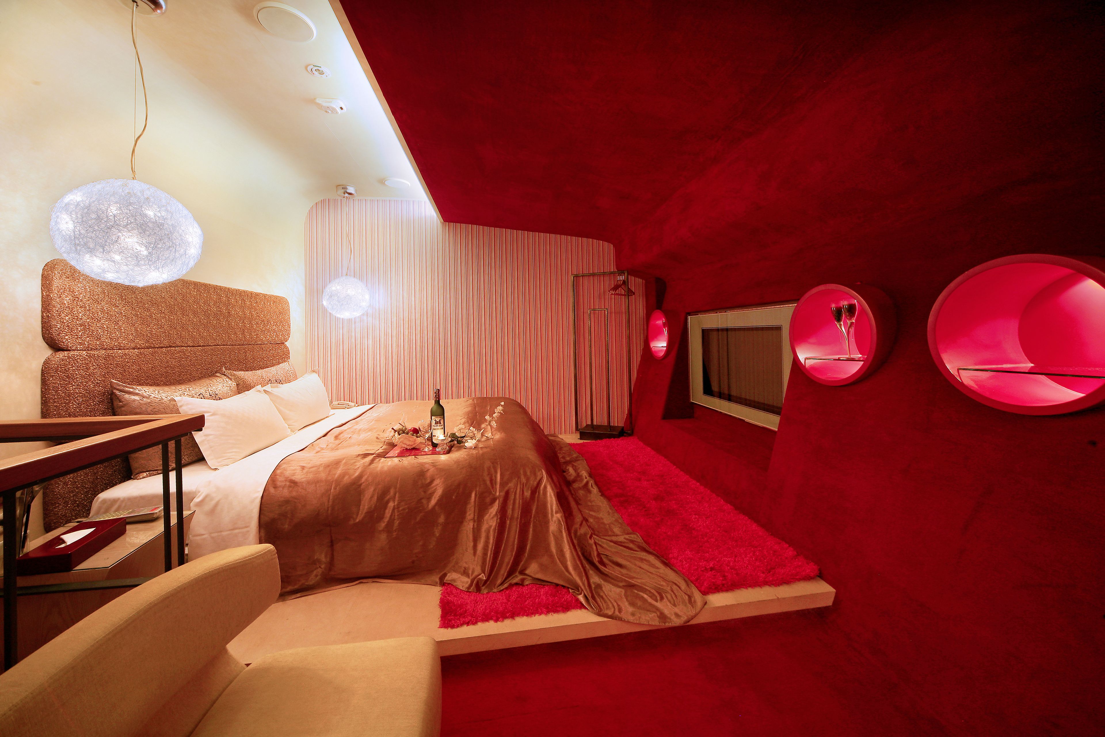 Un dormitorio moderno con una alfombra roja, una cama con cabecera marrón y una mesita de noche con una botella y flores.