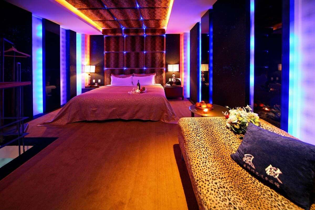 A modern hotel room with a large bed, a sofa, and a nightstand with a lamp.