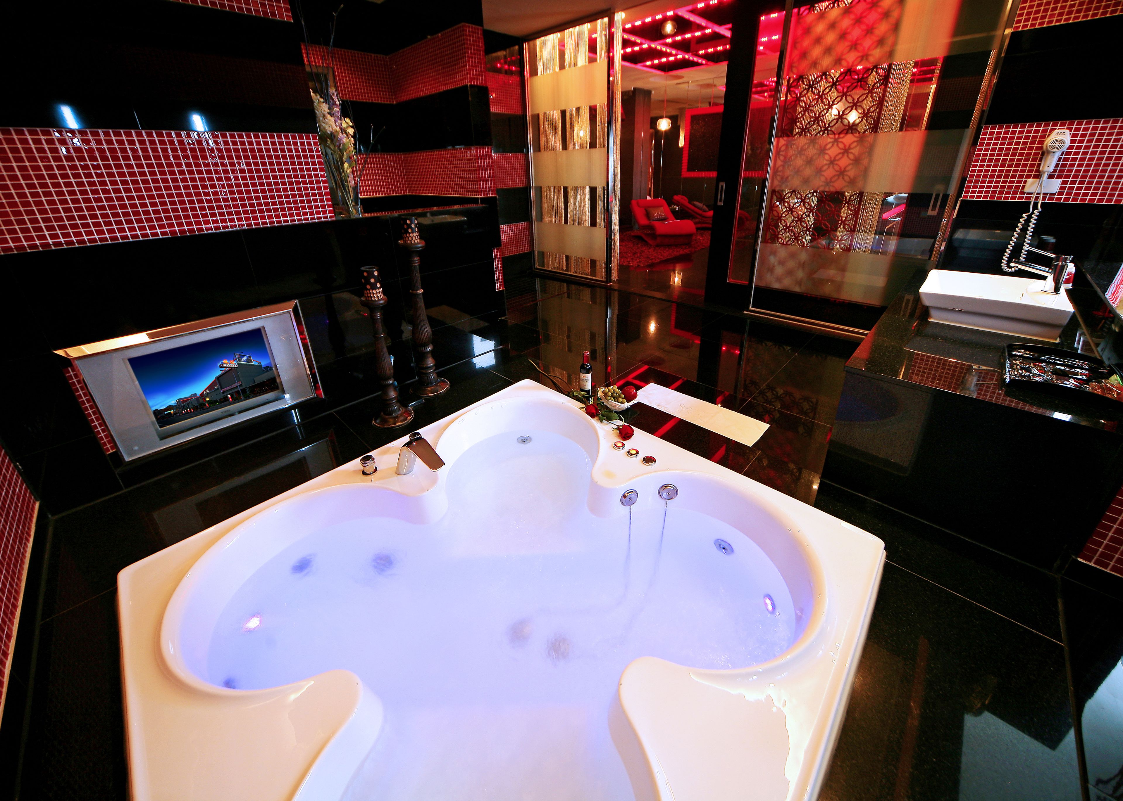 A modern bathroom with a large bathtub, a mirror, and a television on the wall.
