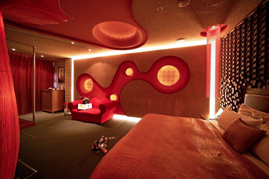 A modern hotel room with a large bed, a red accent chair, and a unique wall design.