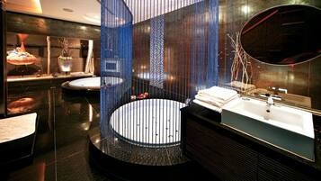 Une salle de bain moderne avec un lavabo central de forme circulaire, deux lavabos latéraux et un grand miroir.