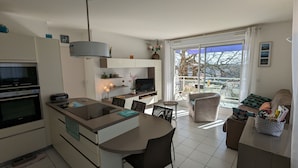 Et moderne køkken med en central ø, spiseplads med stole og en sofa med udsigt.