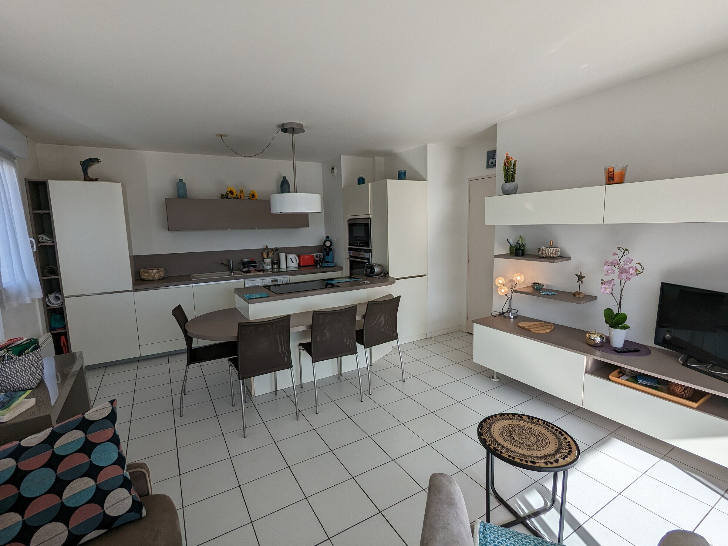 A modern kitchen with white cabinets, a dining area with a table and chairs, and a living area with a TV and decorative items.