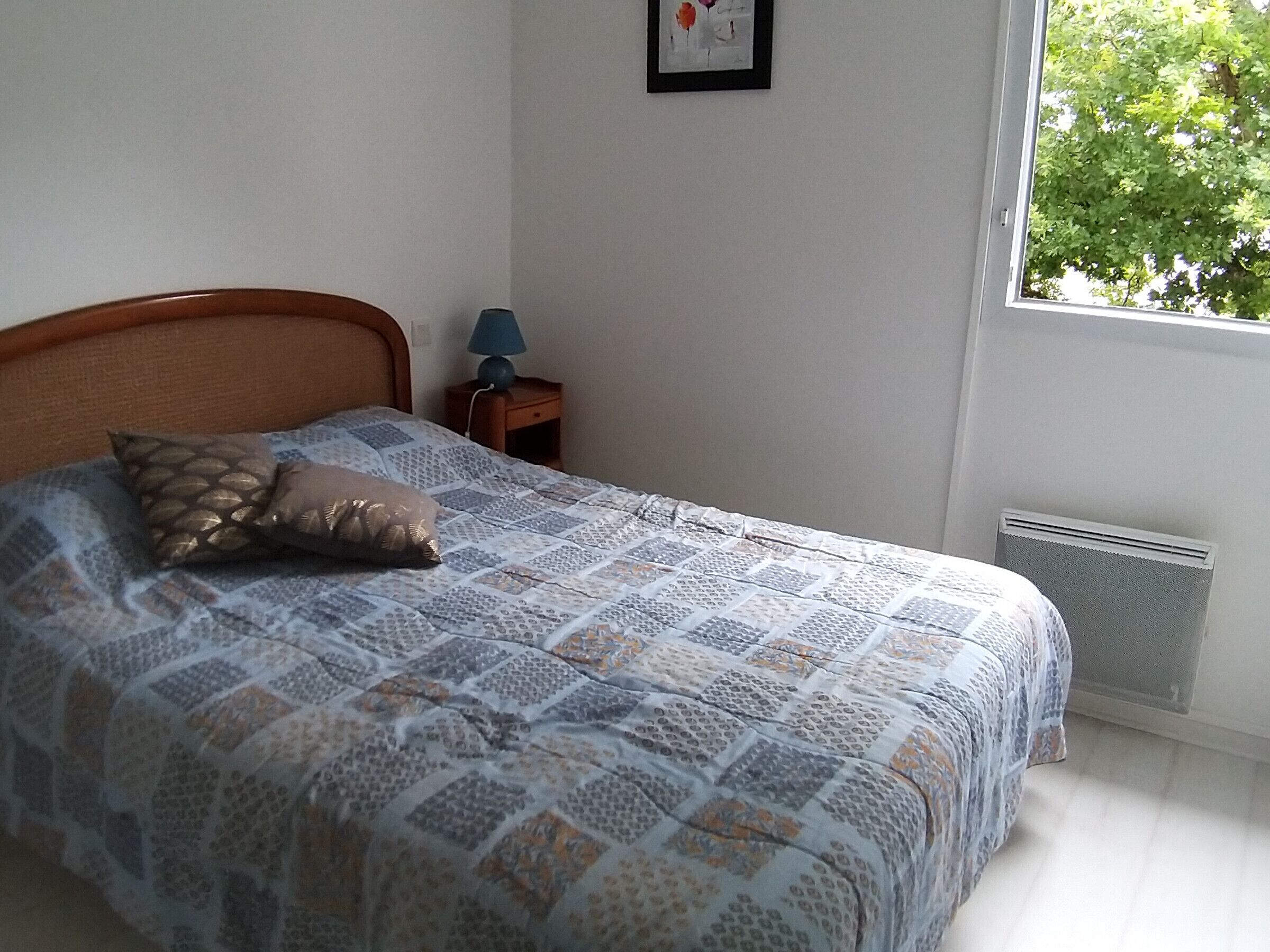 A bedroom with a bed, a nightstand, a lamp, and a window with a view of trees.