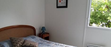 A bedroom with a bed, a nightstand, a lamp, and a window with a view of trees.
