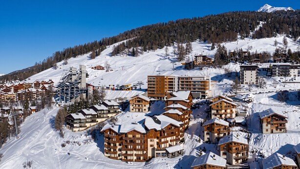 A snow-covered mountain resort with wooden buildings, ski lifts, and a clear blue sky. - Homerez - Studio in Vallandry (Vallandry)
