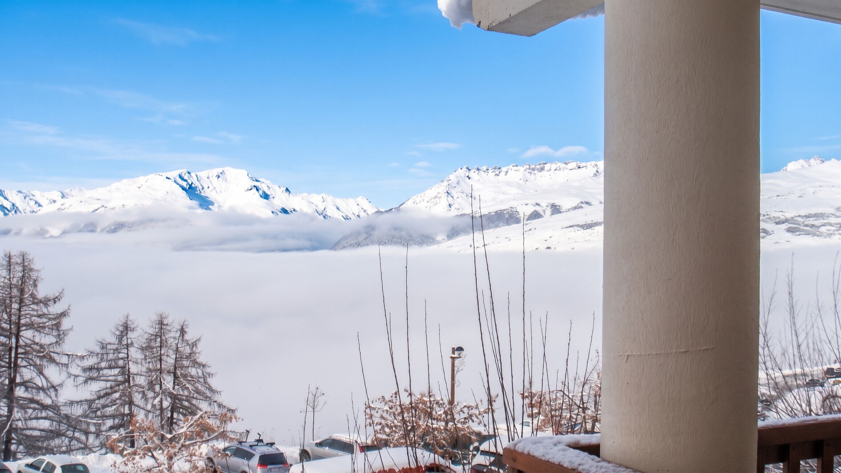 A snowy mountain landscape with a clear sky, a wooden structure, and parked cars.
