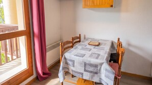 A room with a table, chairs, a window with curtains, a mounted TV, and a hanging light fixture. - Homerez - Studio in Vallandry (Vallandry)