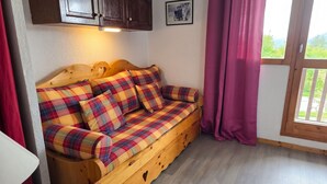 A wooden sofa with plaid cushions in a room with a wooden ceiling, a window with curtains, and a picture on the wall. - Homerez - Studio in Vallandry (Vallandry)