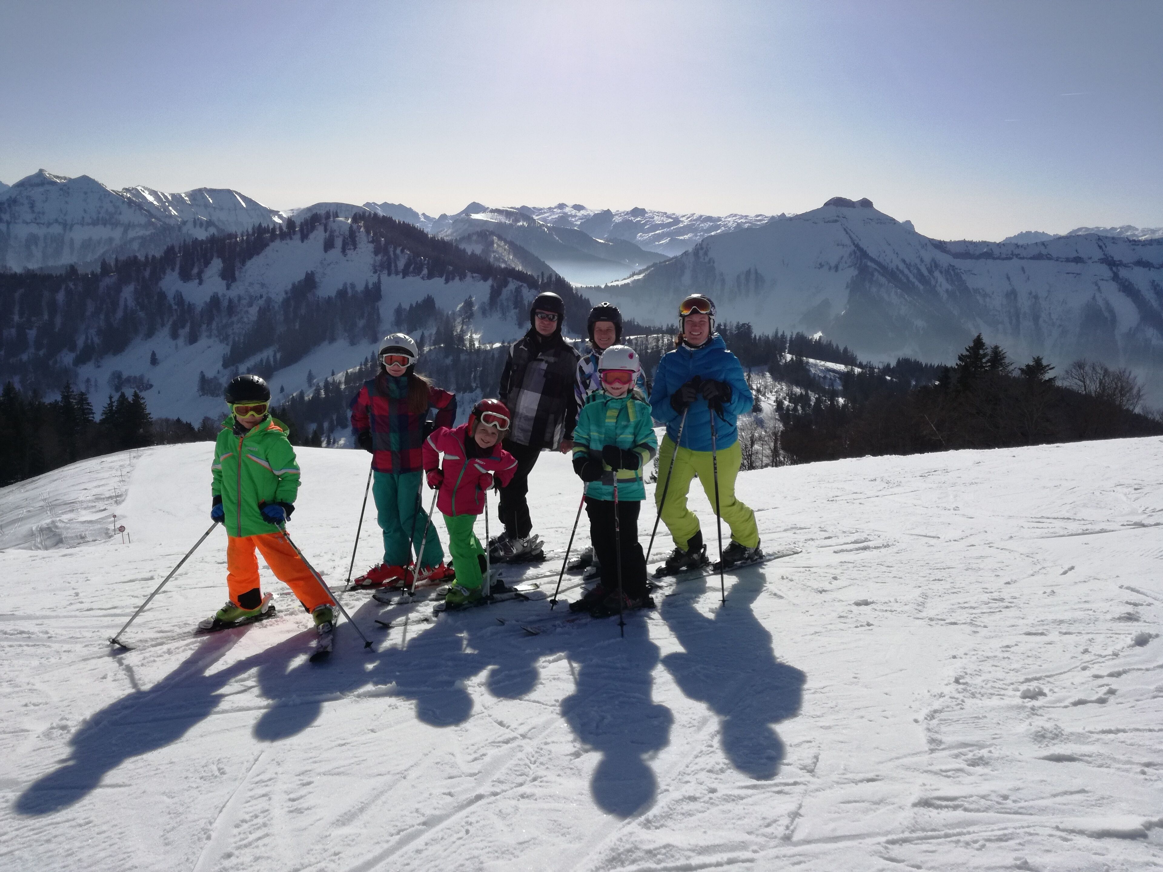 A group of people on a snowy mountain with ski equipment, standing on a flat area with a mountain range in the background.