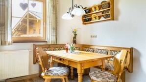 A wooden dining table with a bench, a radiator, a window with heart decorations, and a shelf with plates. - Reitlhof – Your Organic Farm Holiday in Salzburg 🏡🌿 (Krispl-Gaissau)