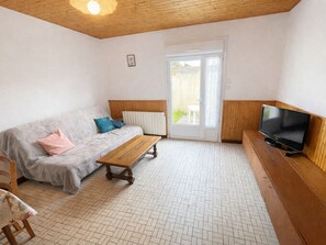 Ein Wohnzimmer mit einer Couch, einem Holztisch, einem Fernseher auf einem Holzschrank und einer Tür, die nach draußen führt.