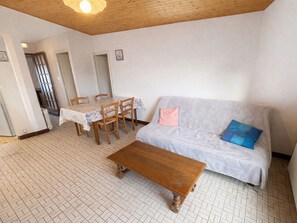 Ein Wohnzimmer mit Couch, Essplatz und Holztisch. Der Boden ist mit Fliesen belegt.