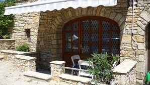 Un edificio de piedra con un amplio ventanal de arco, un espacio de estar techado al aire libre y una planta en maceta.