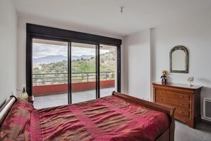 Ein Schlafzimmer mit großem Fenster, einem Bett, einem Schminktisch und einem Spiegel.