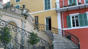 A staircase with ornate black iron railings leading to a building with green shutters and a yellow facade. - Casa San Ghjisé (Bastia)