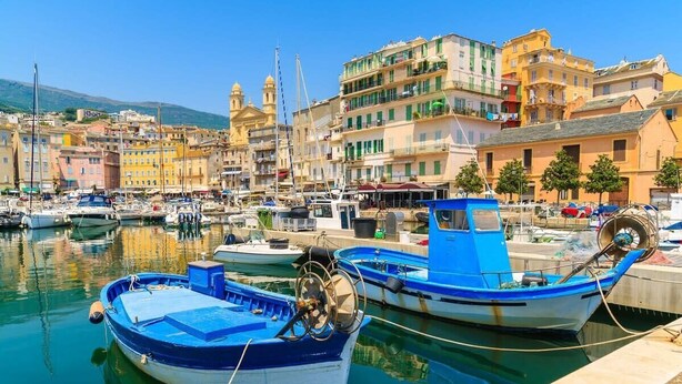 A marina with boats docked, a waterfront promenade, and colorful buildings in the background. - Casa San Ghjisé (Bastia)