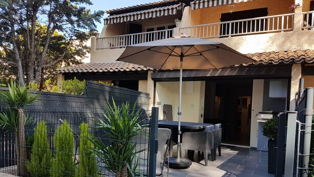 Une terrasse extérieure avec une table et des chaises, un grand parasol et un mur de pierre agrémenté de plantes.