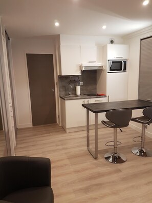 A compact kitchen with white cabinets, a microwave, a sink, and a small countertop. There is a dining table with four chairs. - Studio Seaside at st cyr sur mer (Saint-Cyr-sur-Mer)